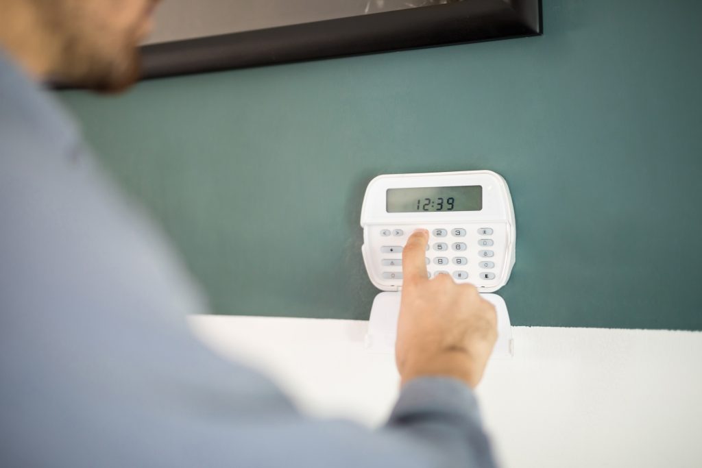 Mężczyzna wprowadza kod na białej klawiaturze systemu alarmowego.
